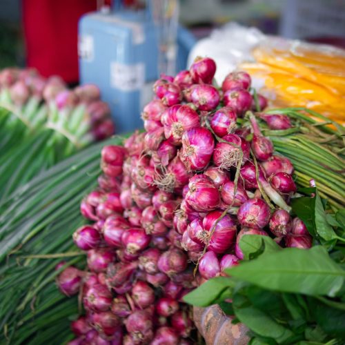 A vibrant display of fresh red onions and greens at a bustling market stall.